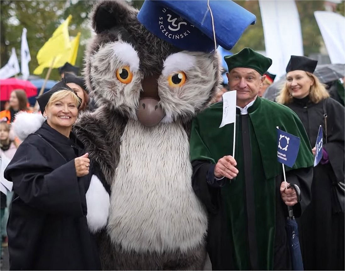 Fotografia przedstawia kostium Sowy zaprojektowany i wykonany przez firmę Elabika, pozujący do fotografii w towarzystwie odświętnie ubranych w togi i birety przedstawicieli władz Uniwersytetu Szczecińskiego 